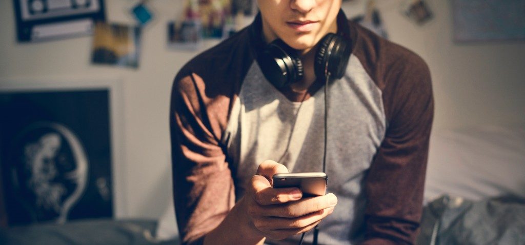teen with headphones and phone in his bedroom