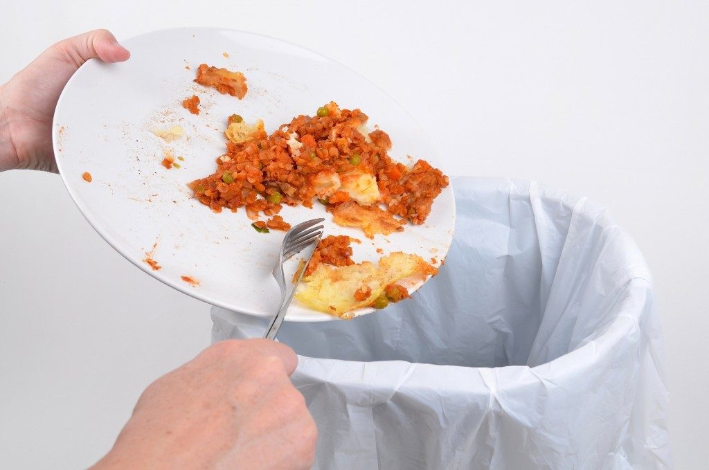 Scraping food waste from a plate into a garbage bin