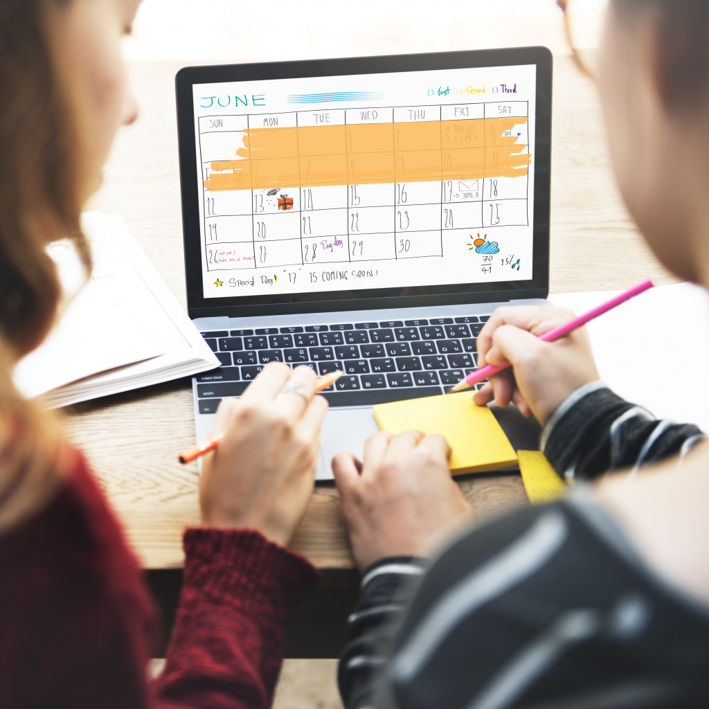 Two people organizing a schedule on a calendar using a laptop