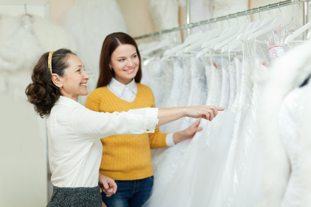 two woman walking through an array of wedding gown