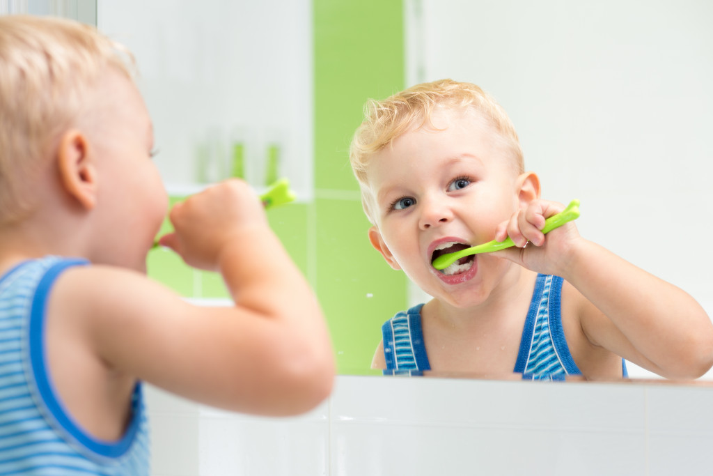 young boy brushing his own teeth in front of mirror