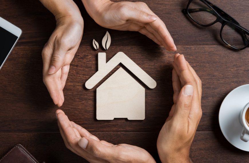 two pairs of hands engulfing a home model with leaves sprouting from the chimney