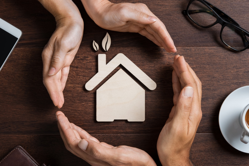 two pairs of hands engulfing a home model with leaves sprouting from the chimney